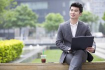 Hombre de negocios chino trabajando con el ordenador portátil en el banco de la calle - foto de stock