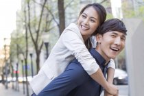 Chinese man holding piggy back girlfriend on street and laughing — Stock Photo