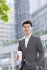 Chinese businessman holding coffee cup on street — Stock Photo