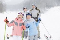 Familia china posando en estación de esquí con bastones de esquí - foto de stock