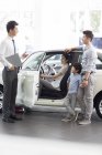 Chinese car seller helping family choosing car in showroom — Stock Photo
