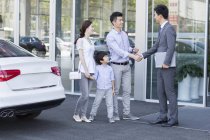 Китайская семья пожимает руку продавцу автомобилей перед выставочным залом — стоковое фото