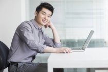Китайский бизнесмен сидит с ноутбуком в офисе — стоковое фото