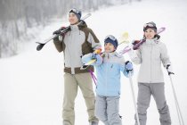 Китайские родители с сыном несут лыжи на плечах на горнолыжном курорте — стоковое фото