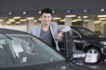Chinese man posing with car on parking lot — Stock Photo