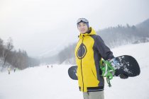 Chinese man posing with snowboard on snowy slope — Stock Photo