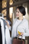 Mature Chinese woman standing with credit card in clothing store — Stock Photo