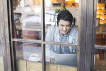 Homem chinês em fones de ouvido usando laptop no café — Fotografia de Stock