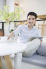 Hombre chino sentado con tableta digital en la cafetería - foto de stock