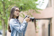 Fotógrafo chinês feminino em pé com câmera digital na rua — Fotografia de Stock