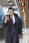 Homme d'affaires chinois marchant à l'aéroport avec passeport et smartphone — Photo de stock