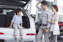 Menino chinês sentado no porta-malas do carro com os pais no showroom — Fotografia de Stock