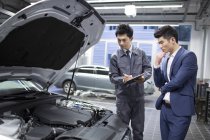 Chinese auto mechanic and car owner looking at engine — Stock Photo