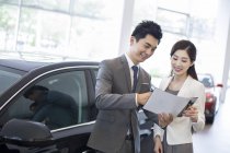 Chinese businesswoman making deal with car seller in showroom — Stock Photo