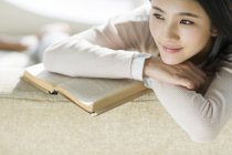 Портрет китайской женщины, сидящей на диване с книгой — стоковое фото