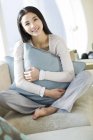 Chinese woman hugging pillow on home interior — Stock Photo