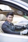 Chinese chauffeur driving car and looking in camera — Stock Photo