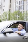 Hombre chino conduciendo e inclinándose fuera del coche - foto de stock