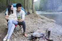 Chinese couple sitting beside campfire with beer — Stock Photo