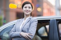 Chinese woman leaning on car and smiling — Stock Photo