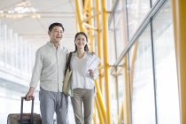 Зрелая китайская пара, идущая в аэропорт с чемоданом — стоковое фото