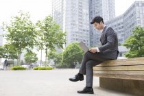 Китайский бизнесмен работает с ноутбуком на уличной скамейке — стоковое фото