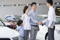 Famiglia cinese che stringe la mano con il venditore di auto nello showroom — Foto stock