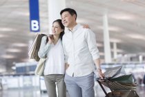 Reifes chinesisches Paar steht mit Einkaufstüten am Flughafen — Stockfoto