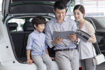 Família chinesa olhando para o catálogo do carro no showroom — Fotografia de Stock