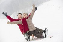 Senior pareja china deslizándose en trineo en la pendiente nevada - foto de stock