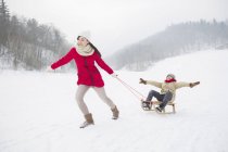 Chinese mother pulling son on sled — Stock Photo