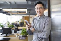 Chinese man holding smartphone in office — Stock Photo
