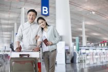 Pareja china madura parada en el aeropuerto con entradas - foto de stock