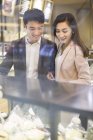 Chinese couple choosing cakes in bakery — Stock Photo
