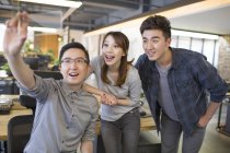 Chinese IT workers holding smartphone model and cheering in office — Stock Photo