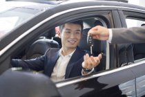 Chinese businessman receiving car keys in showroom — Stock Photo