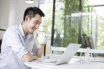 Uomo cinese seduto con laptop e tazza di caffè — Foto stock