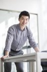 Китайский бизнесмен, опираясь на стол и улыбаясь — стоковое фото