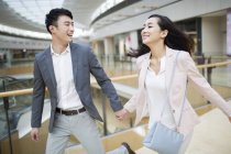 Casal chinês de mãos dadas e correndo em shopping — Fotografia de Stock