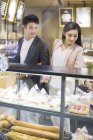 Chinese couple choosing cakes in bakery — Stock Photo