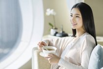Китаянка ест кашу на диване в интерьере дома — стоковое фото