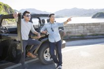 Chinese men leaning on car in suburbs and pointing — Stock Photo