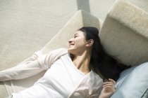 Happy Chinese woman lying down on sofa in sunlight — Stock Photo