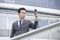 Hombre de negocios chino tomando fotos con teléfono inteligente - foto de stock