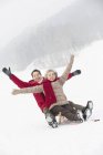 Senior Chinese couple sliding on sled on snowy slope — Stock Photo