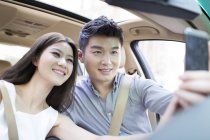 Chinese couple sitting in car and taking selfie — Stock Photo