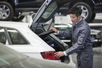 Mécanicien automobile chinois regardant dans le coffre de la voiture dans l'atelier de réparation — Photo de stock