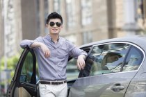 Hombre chino de pie frente al coche en la ciudad - foto de stock