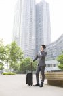Китайский бизнесмен разговаривает по телефону с чемоданом — стоковое фото