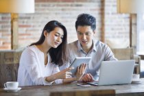 Chinese man and woman using digital tablet and laptop in cafe — Stock Photo